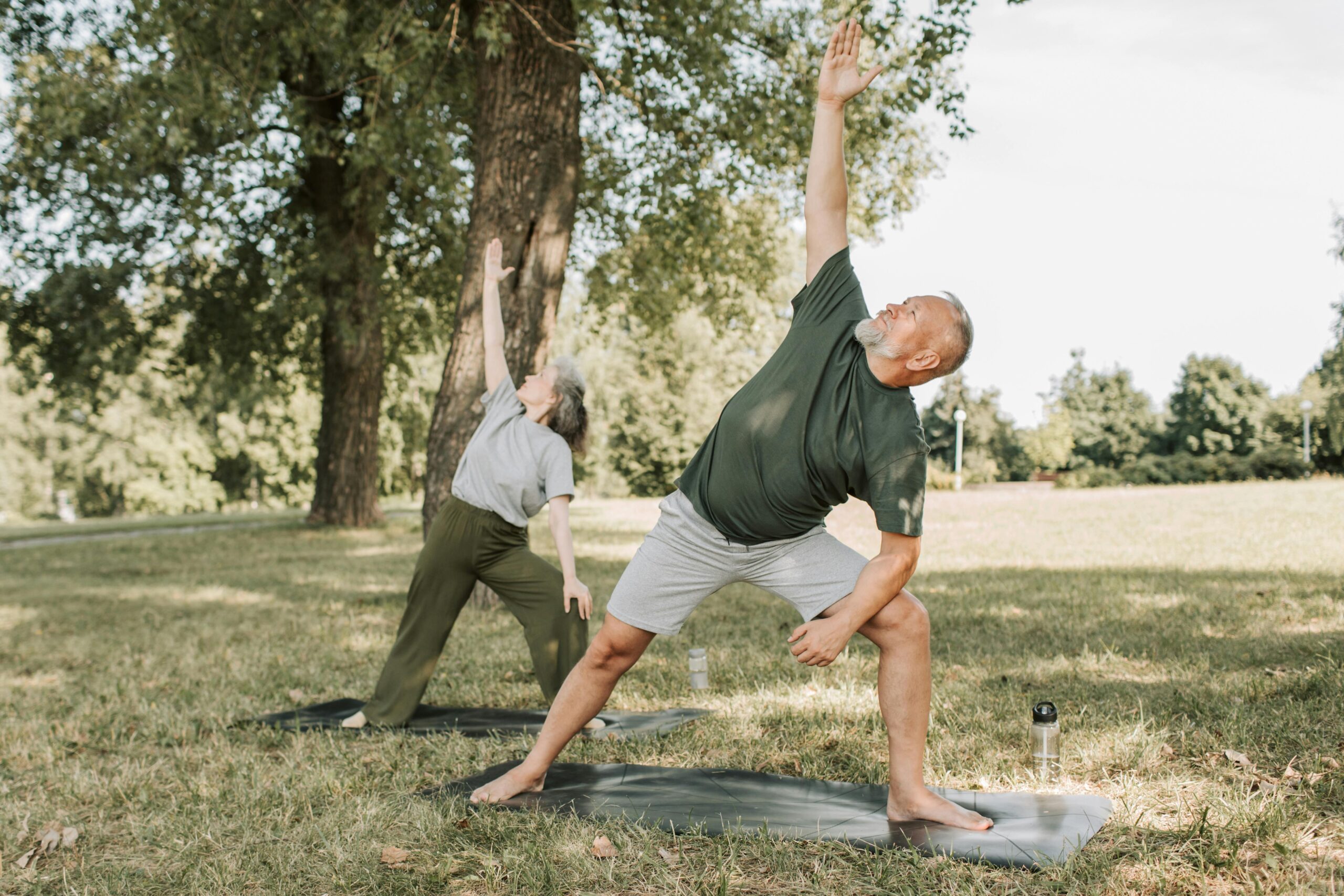 an old man and an old woman doing yoga in a park on a sunny day